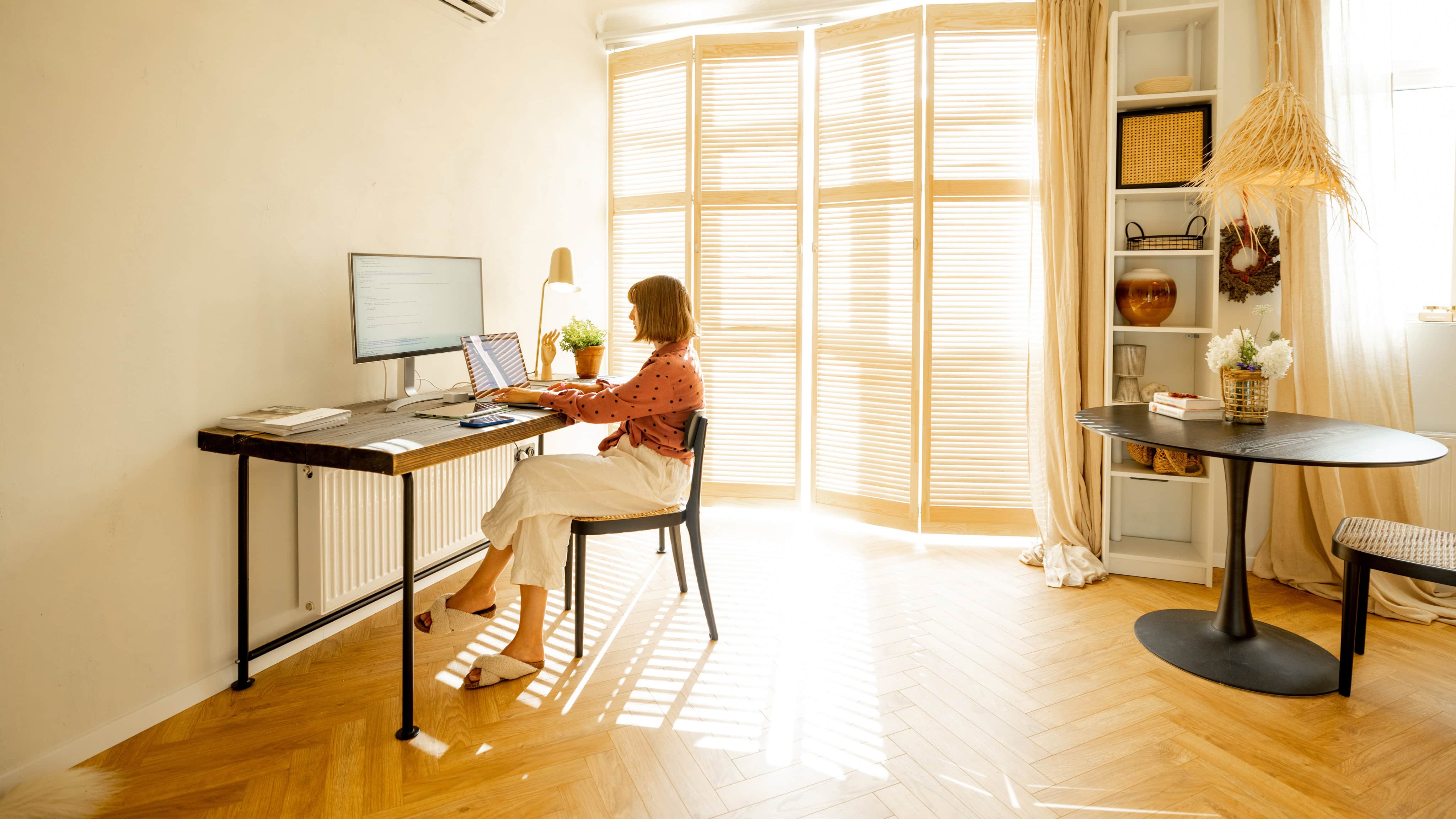 Frau arbeitet am Computer, während sie an einem gemütlichen Arbeitsplatz im sonnigen Wohnzimmer zu Hause sitzt. Konzept der Remote-Arbeit von zu Hause aus Büro.